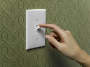 Woman turning off light switch on green wallpapered wall, close-up