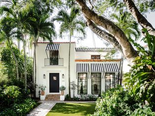 White house with black trim and striped black and white window awnings.