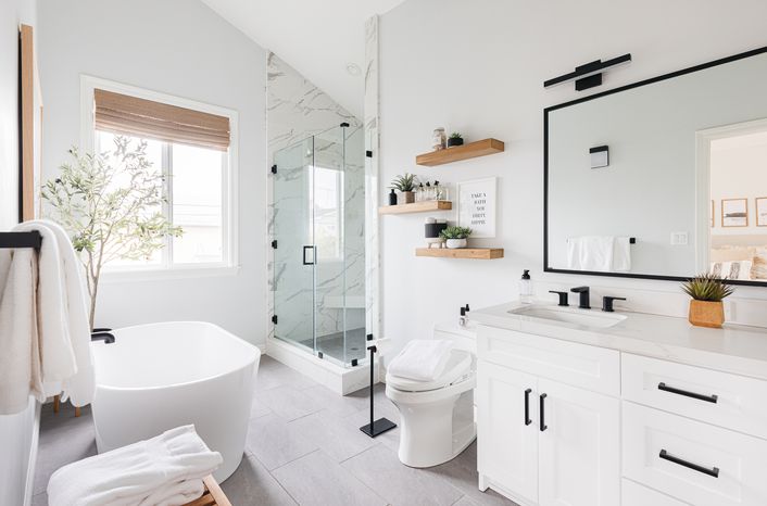 A mostly white bathroom coupled with black hardware and floating wood shelves