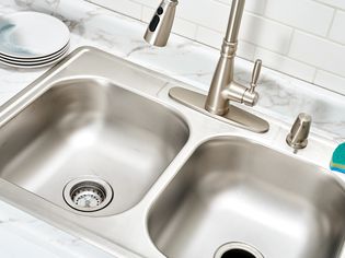 Double sink surrounded with marble countertop with sponge and stacked dishes