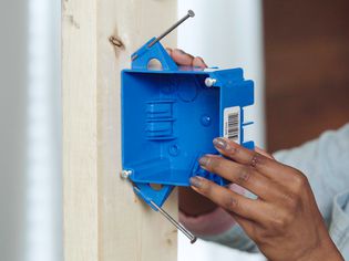 Electrical junction box being nailed to wooden post for installation