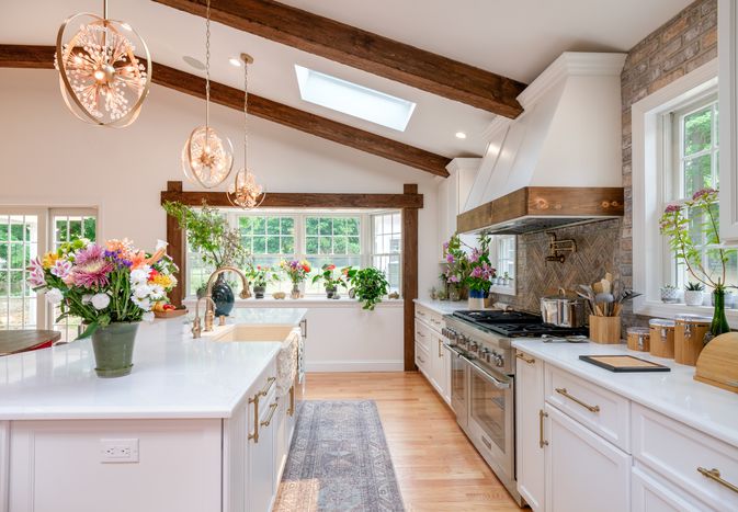 An airy and modern farmhouse kitchen with exposed natural stone walls, wooden beams, and white glossy countertops