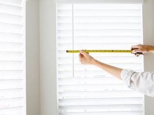 White inside-mount window blinds measured with yellow tape measure closeup