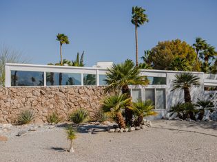 White modern home in desert landscaping and palms in front