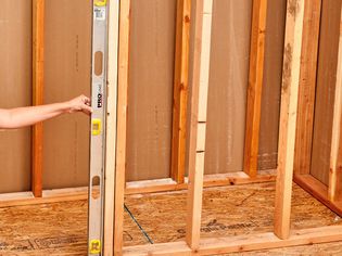 A person holding a level against a wall stud.