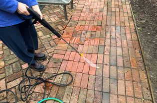 A person uses the Sun Joe SPX3500 Brushless Induction Electric Pressure Washer to clean bricks outside