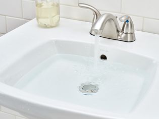 Bathroom faucet running water filling up sink and covering overflow hole