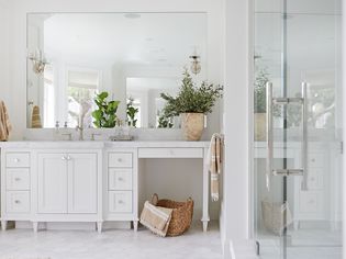 A bathroom that's all-white, aside from a few beige accents and a couple green plants