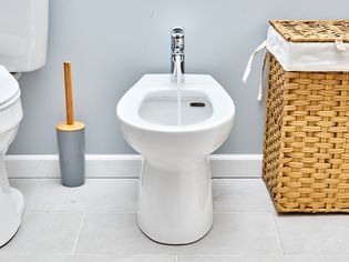 Bidet running with stream of water between toilet and wicker hamper